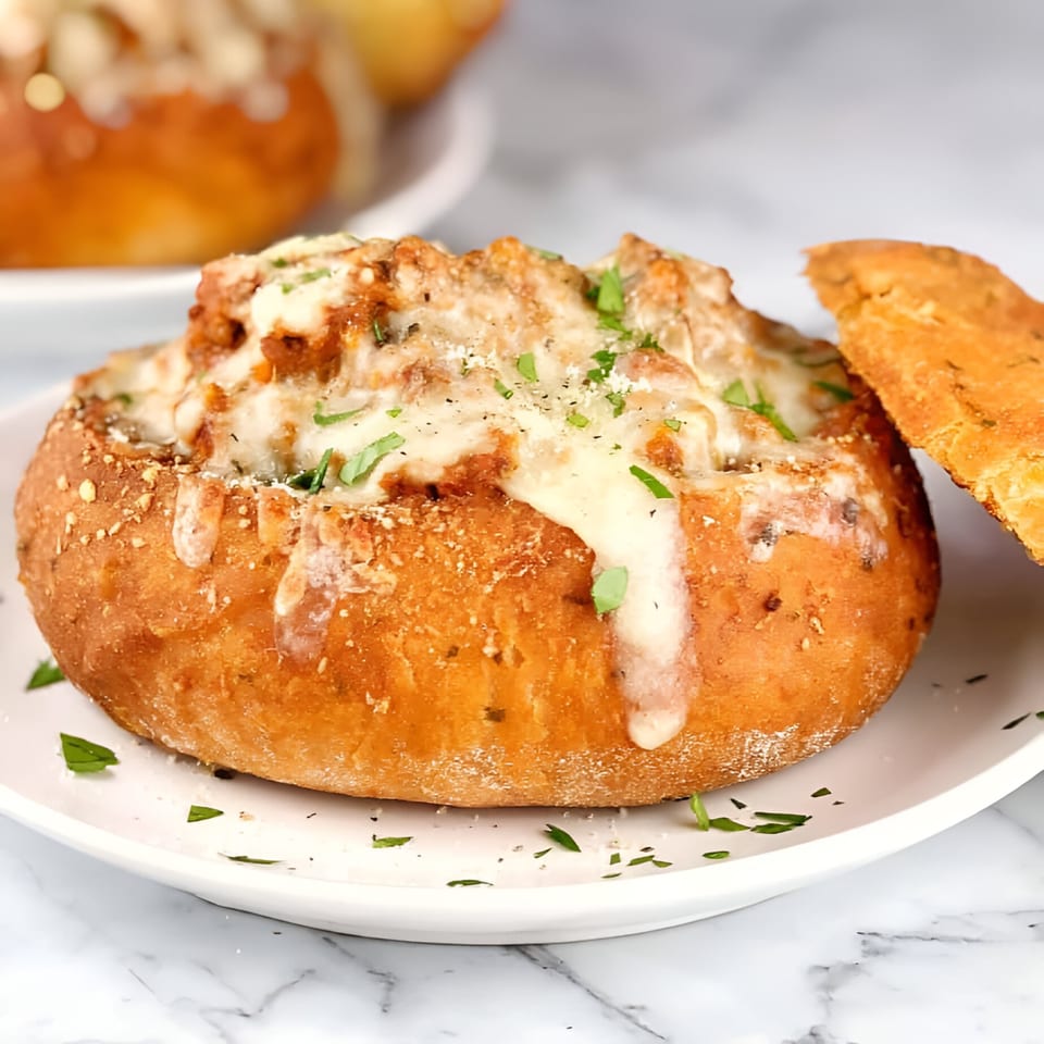Cheesy seafood dip in a bread bowl, garnished with parsley, on a white plate.